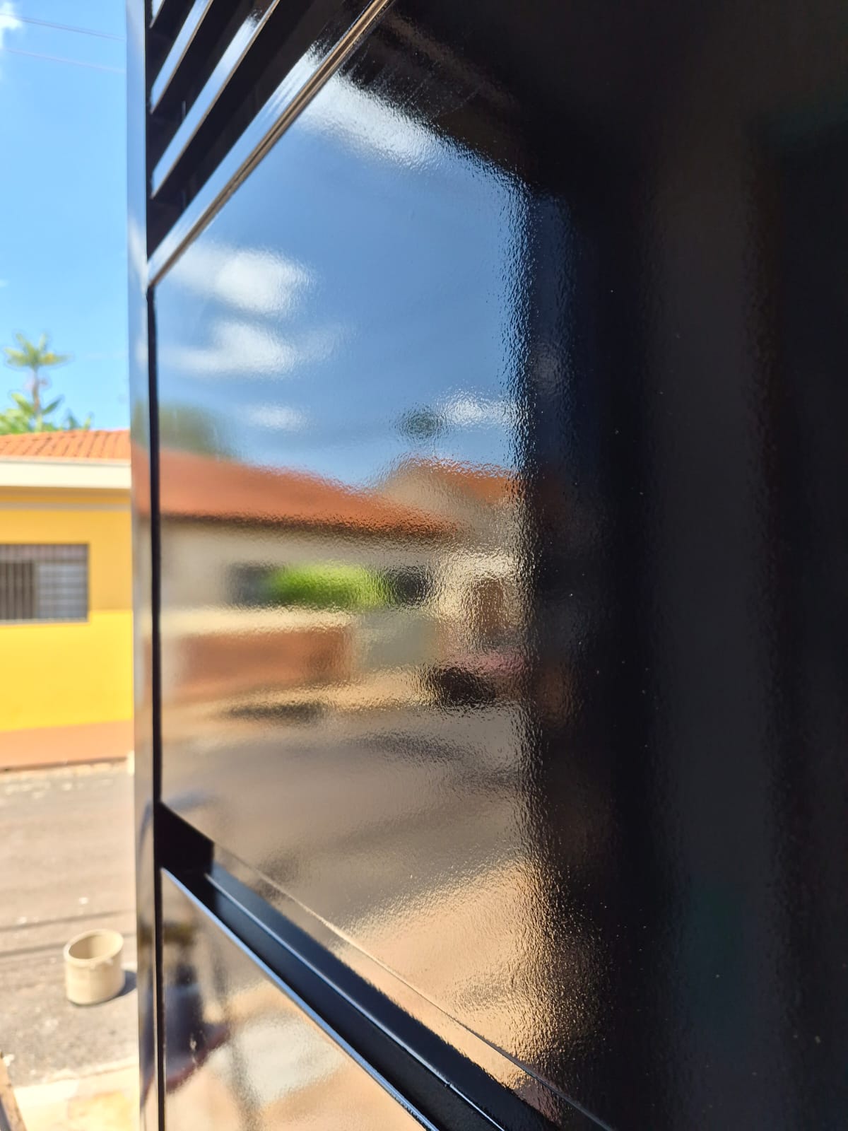 Portão pintado de preto com acabamento brilhante refletindo a rua como um espelho